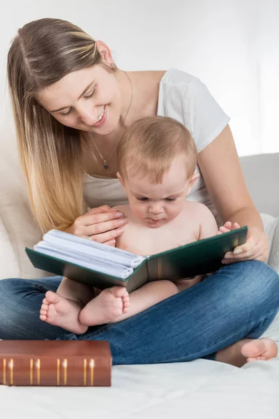 Bonito 1 ano de idade bebê menino sentado no colo mães e lendo grande livro velho — Fotografia de Stock