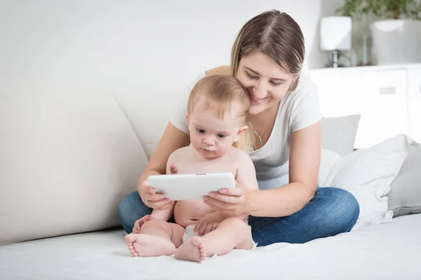 Ung mamma sitter på sängen med hennes baby son och visar honom karikatyrerna på digitala tablett — Stockfoto