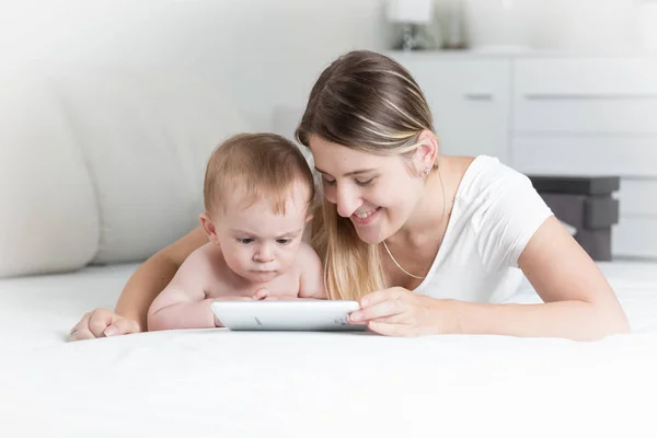 Retrato de la madre sonriente con el bebé acostado en la cama y usando tableta digital —  Fotos de Stock