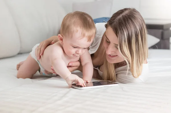 Schattige babyjongen in luiers liggend op bed met moeder en het gebruik van digitale tablet — Stockfoto