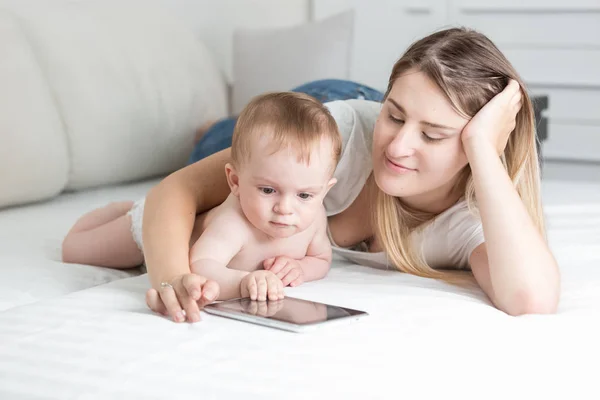 Porträtt av leende ung mamma liggande med sin baby son titta på tecknade filmer om digital tablett — Stockfoto