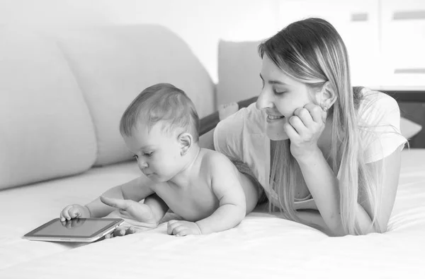Svartvita porträtt av småbarn pojke liggande med mamma på sängen och titta på TV på digitala tablett — Stockfoto