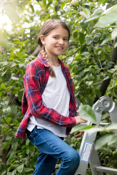 Портрет красивой улыбающейся девочки-подростка, стоящей на вершине стремянки в саду — стоковое фото