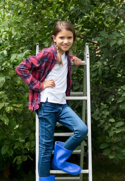 Retrato de menina bonita em camisa quadriculada vermelha e botas wellington na escada rolante no jardim — Fotografia de Stock