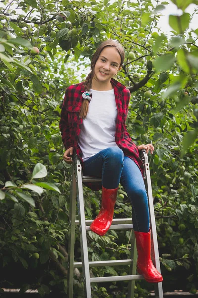 Tónusú fénykép mosolygó tizenéves lány piros gumicsizma Utaslépcsők kert tetején ül — Stock Fotó