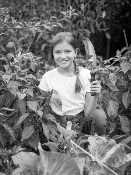 Черно-белый портрет улыбающейся девочки-подростка, сидящей в саду и держащей лопатку — стоковое фото