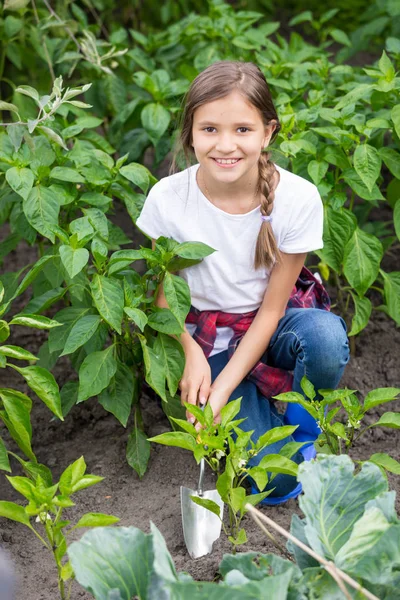 Portrait of beautiful smiling girl spudding garden bed with growing vegetables with trowel — Stock Photo, Image