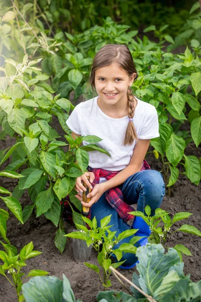 Portrait of beautiful girlspudding soil with trowel between rows of growing vegetables in garden — Stock Photo, Image
