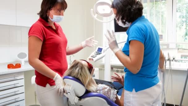 4 k beelden van jonge vrouw in tandheelkundige stoel zitten en praten met tandarts vóór tanden whitening — Stockvideo