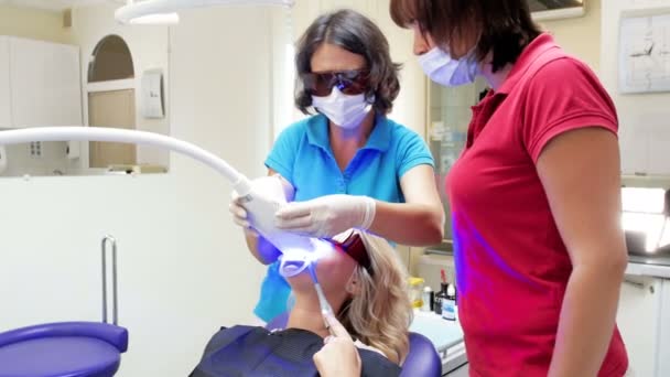 女性の歯科医がホワイトニングの手順のための特別な紫外線ランプをオンの 4 k 映像 — ストック動画