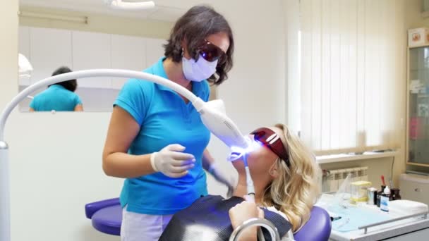 4 k wideo dentysty mówi do pacjenta leżącego w fotelu u dentysty, podczas procedury do wybielania zębów — Wideo stockowe