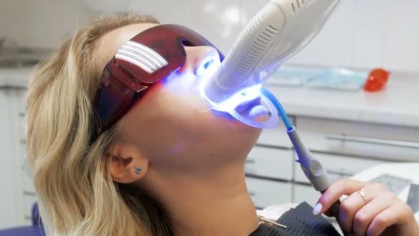 Primer plano 4k video de mujer joven acostada en silla de dentista con lámpara UV para curar dientes — Vídeo de stock