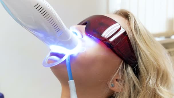 Gros plan 4k vidéo de blonde jeune femme couchée dans la chaise du dentiste pendant la procédure de blanchiment des dents — Video