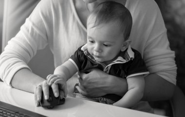 Ofiste çalışan ve bilgisayar fare tutan anne kucağına oturan bebek çocuk fotoğrafı siyah-beyaz