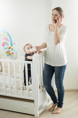 Genç kadın telefonla süt ile bebek oğlu beslerken söz meşgul