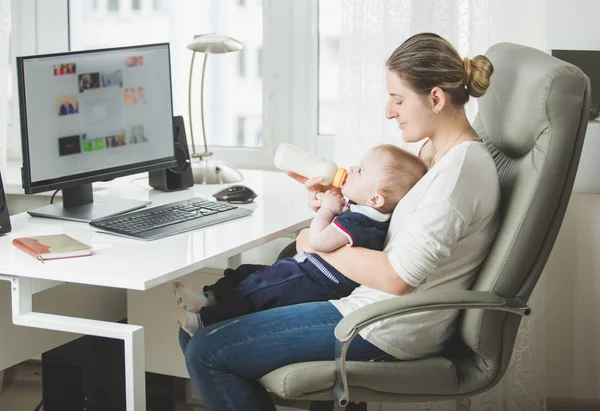 Vacker ung kvinna som arbetar på kontor och letar efter hennes baby son — Stockfoto