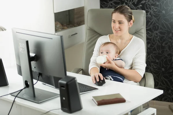 Porträt einer jungen selbstständigen Frau, die zu Hause arbeitet und ihrem kleinen Sohn Milch gibt — Stockfoto