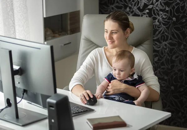 Cute baby boy sitting on mothers lap while she is working at office — Stock Photo, Image