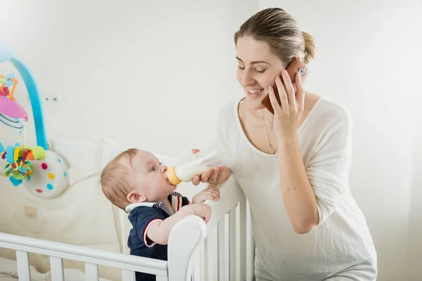 Retrato de una joven empresaria sonriente hablando por teléfono y alimentando a su pequeño hijo —  Fotos de Stock