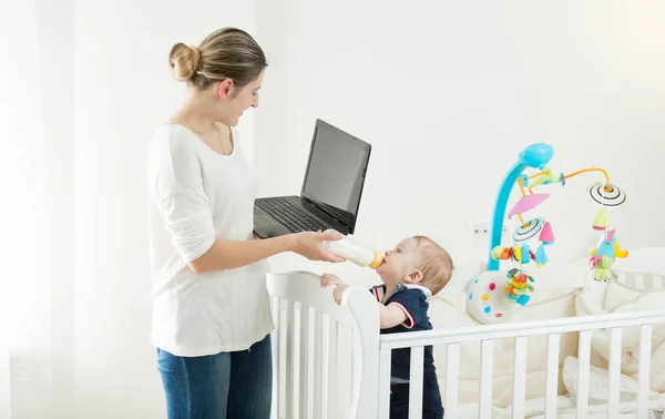 노트북에 노력 하 고 그녀의 아기 아들에 게 우유를 주는 젊은 바쁜 여자의 초상화 — 스톡 사진