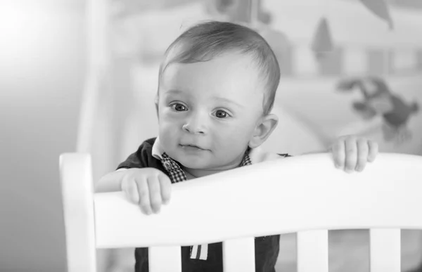 Black and white image of adorable baby boy standing in cot — Stock Photo, Image