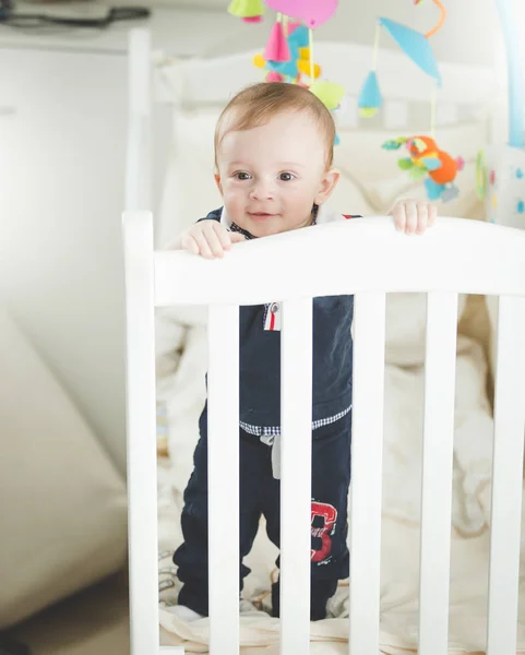 Portrait of adroable 1 year old baby boy standing in white wooden crib — Stock Photo, Image