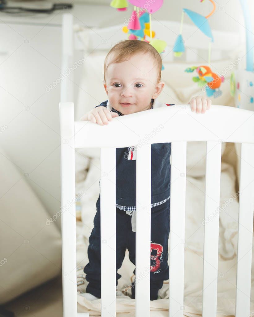 Portrait of adroable 1 year old baby boy standing in white wooden crib