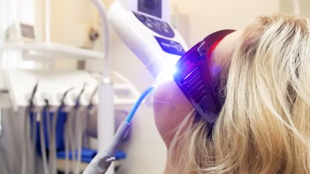 Closeup 4k video van jonge vrouw liggend in tandheelkundige stoel tijdens tanden whitening procedure met UV-lamp — Stockvideo