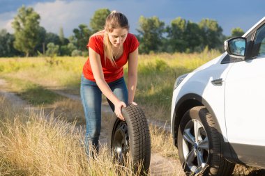 Genç kadın kırsal yolda stepne kırık arabası için haddeleme