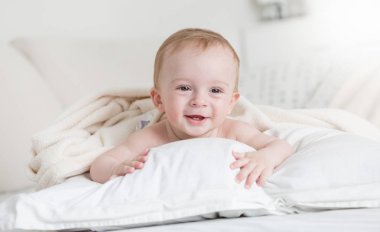 Büyük beyaz yastık yatakta yatan sevimli gülümseyen bebek çocuk portresi