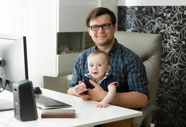 Portret uśmiechający się freelancer mężczyzna młody siedzi w domowym biurze i trzymający syna 1 roku życia dziecka — Zdjęcie stockowe