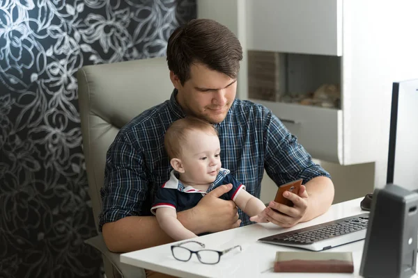 Retrato del joven hipster sentado con su hijo bebé en la oficina y mirando el teléfono inteligente — Foto de Stock