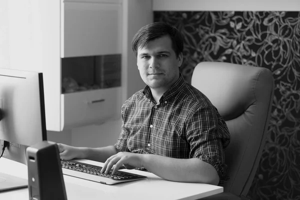 Черно-белый портрет молодого человека, работающего за компьютером в домашнем офисе — стоковое фото