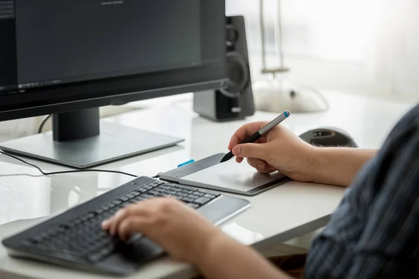 Closeup image of young man designer siting behind computer and working with graphic tablet