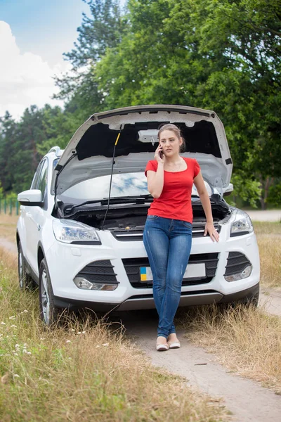 Young woman leaning on broken car in field and talking by phone — Stock Photo, Image