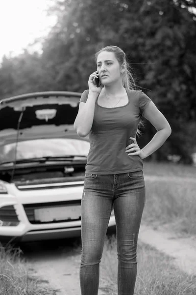 Black and white image of young woman calling car assistance service in the field