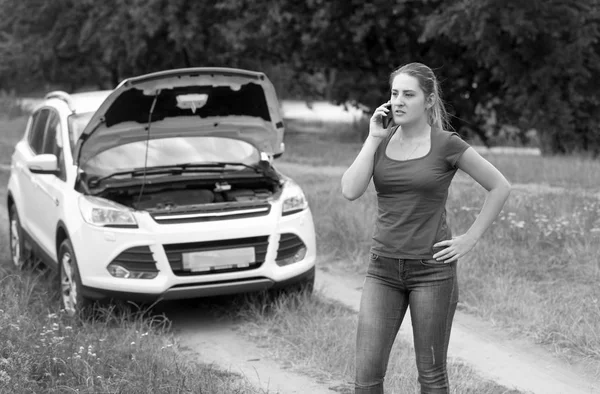 Black and white image of angry young woman talking to car service beacuse of her broken car — Stock Photo, Image