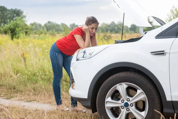 Triste femme appuyé sur la voiture cassée dans le champ et en regardant le moteur — Photo