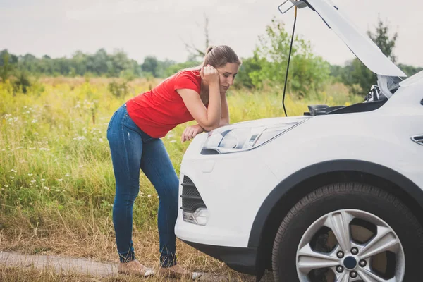 Foto tonica di giovane donna in piedi in auto rotta sulla strada di campagna e guardando il motore surriscaldato — Foto Stock