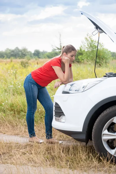 Triest jonge vrouw leunend op gebroken auto in veld en wachten op hulp — Stockfoto