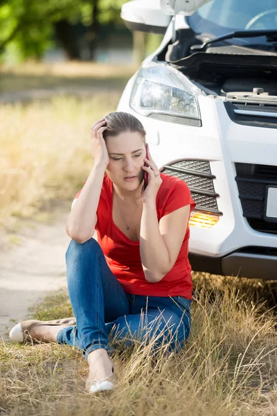 Young crying woman sitting at her broken car in field and calling auto service — Stock Photo, Image
