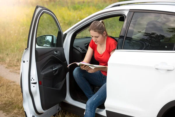 Retrato de mujer joven se perdió en la carretera rural en coche en busca de la ruta correcta en el mapa —  Fotos de Stock