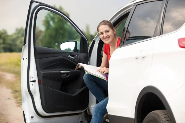 Portret van lachende jonge vrouw reizen in de auto met behulp van papieren kaart — Stockfoto