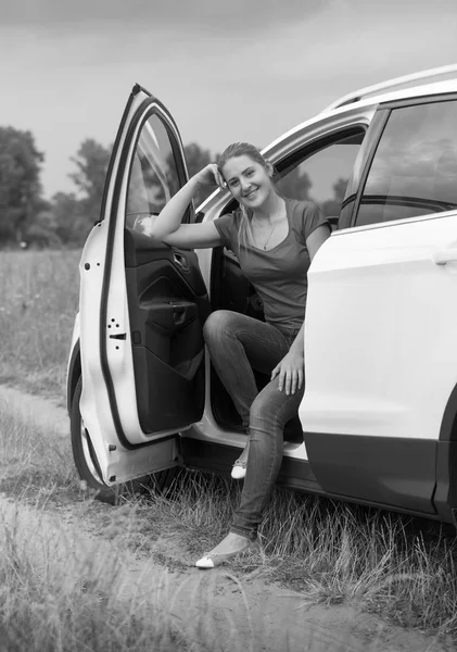 Black and white image of smiling young woman traveling by car opened door looking in camera — Stock Photo, Image