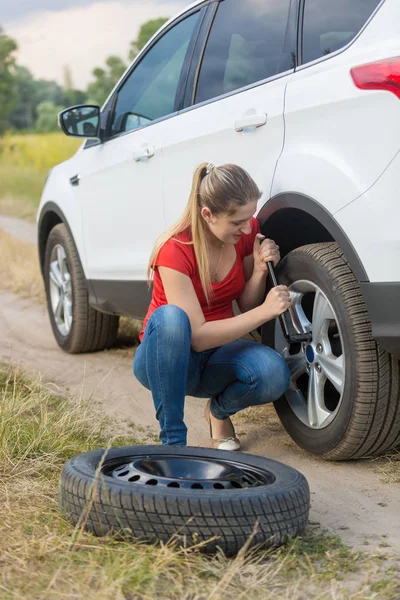 Mujer joven desenroscar tuercas en la rueda de su coche roto con neumático plano —  Fotos de Stock