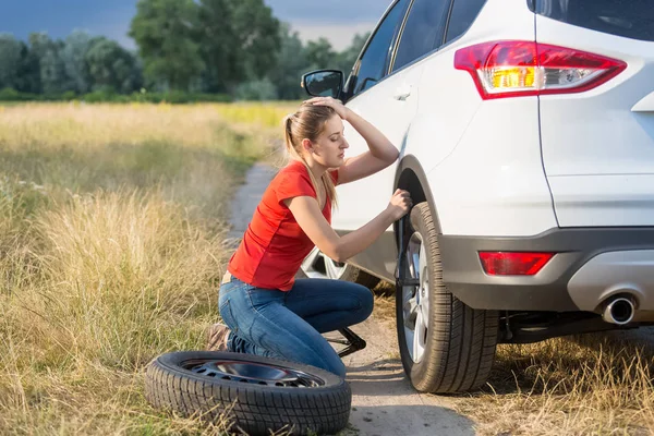 Mujer joven luchando para cambiar neumático de coche plano en la carretera rural — Foto de Stock