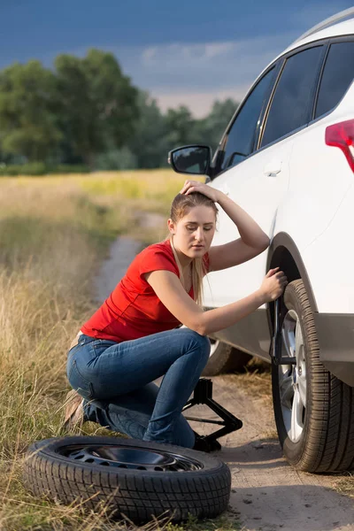Jovem sentada em seu carro com pneu furado tentando desaparafusar porcas da roda — Fotografia de Stock