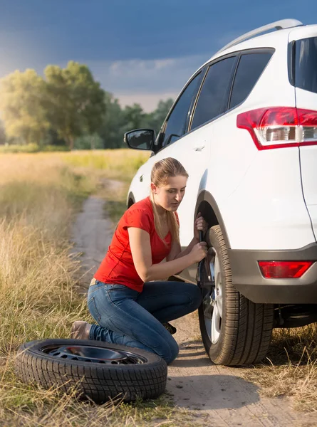 Mujer joven usando gato de coche para levantar su coche roto en el campo — Foto de Stock
