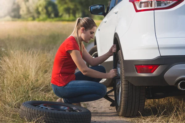 Toned image of young woman changing car flat tire with spare field in field — Stock Photo, Image