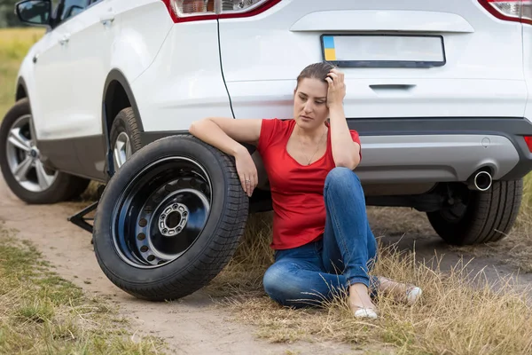 フィールドでパンクしたタイヤが付いている車に寄りかかっての若い女性の肖像画 — ストック写真